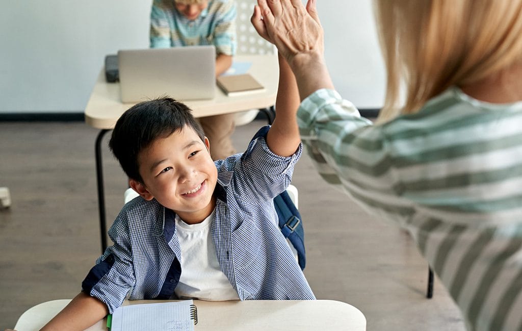Garoto asiático feliz dando mais cinco para professora na aula em sala de aula. Professor encorajando chinês alegre ajudando estudante criança dando apoio durante a aula do ensino fundamental.