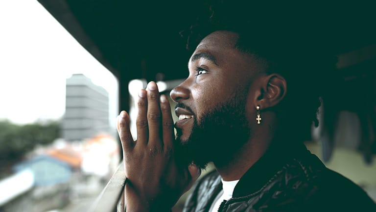 Um jovem negro espiritual em profunda ORAÇÃO meditativa, afro-americano contemplativo de 20 anos abrindo os olhos e sorrindo com ESPERANÇA e FÉ. Conceito de GRATIDÃO