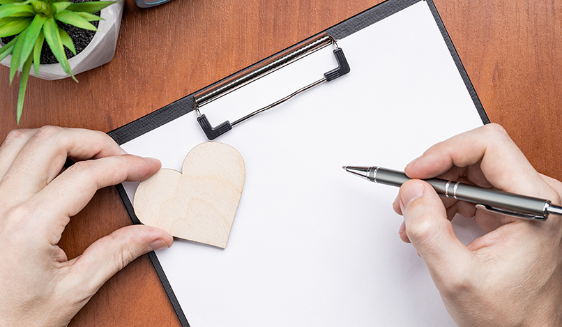Prancheta em branco sobre mesa de madeira, decorada com um símbolo de coração. Vista de cima. Modelo de cartão de metas para o Dia dos Namorados. Conceito de contrato de amor.
