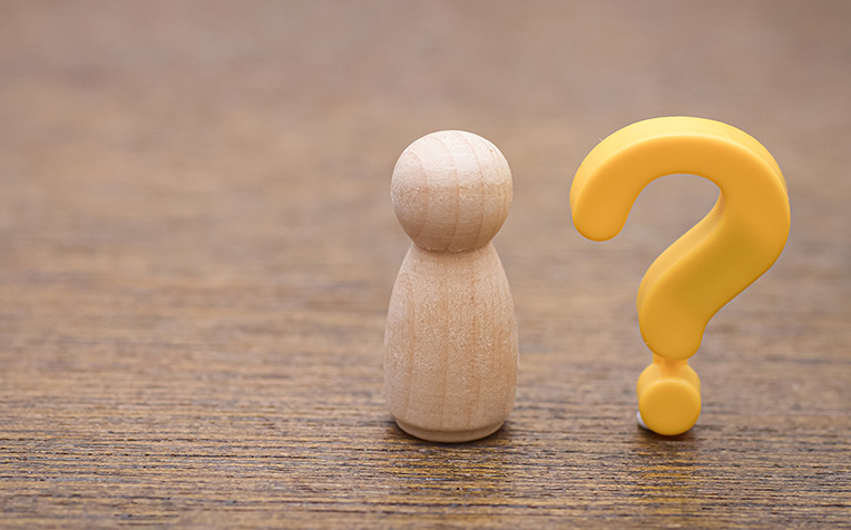 Uma simples boneca de madeira com um ponto de interrogação amarelo simboliza as experiências humanas universais da dúvida, da identidade pessoal e da busca por respostas.